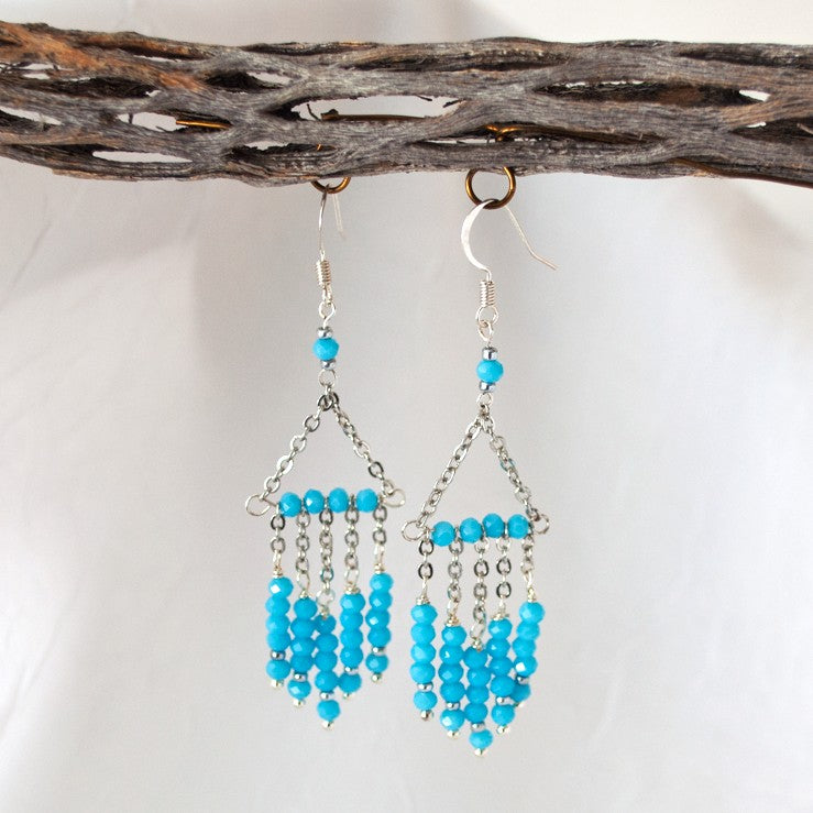 Turquoise color chandelier earrings with faceted rondelle bead strands and stainless steel chain, hanging from driftwood against a neutral background