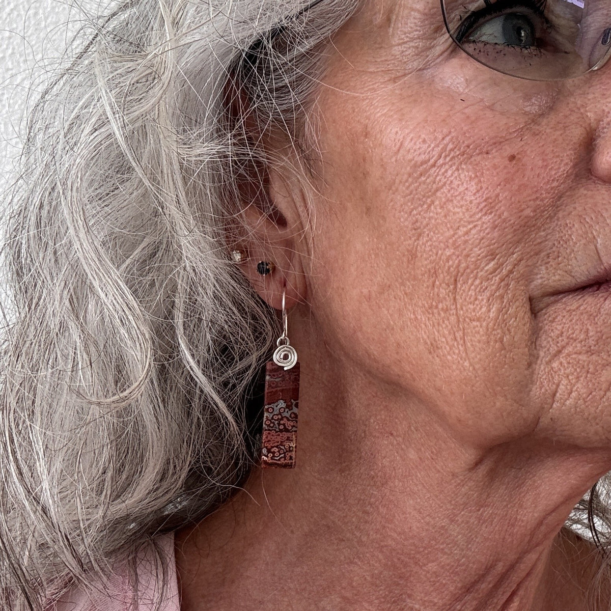 	Brecciated jasper earring with silver-tone handcrafted swirl bail and hammered ear wire shown worn on model with silver hair