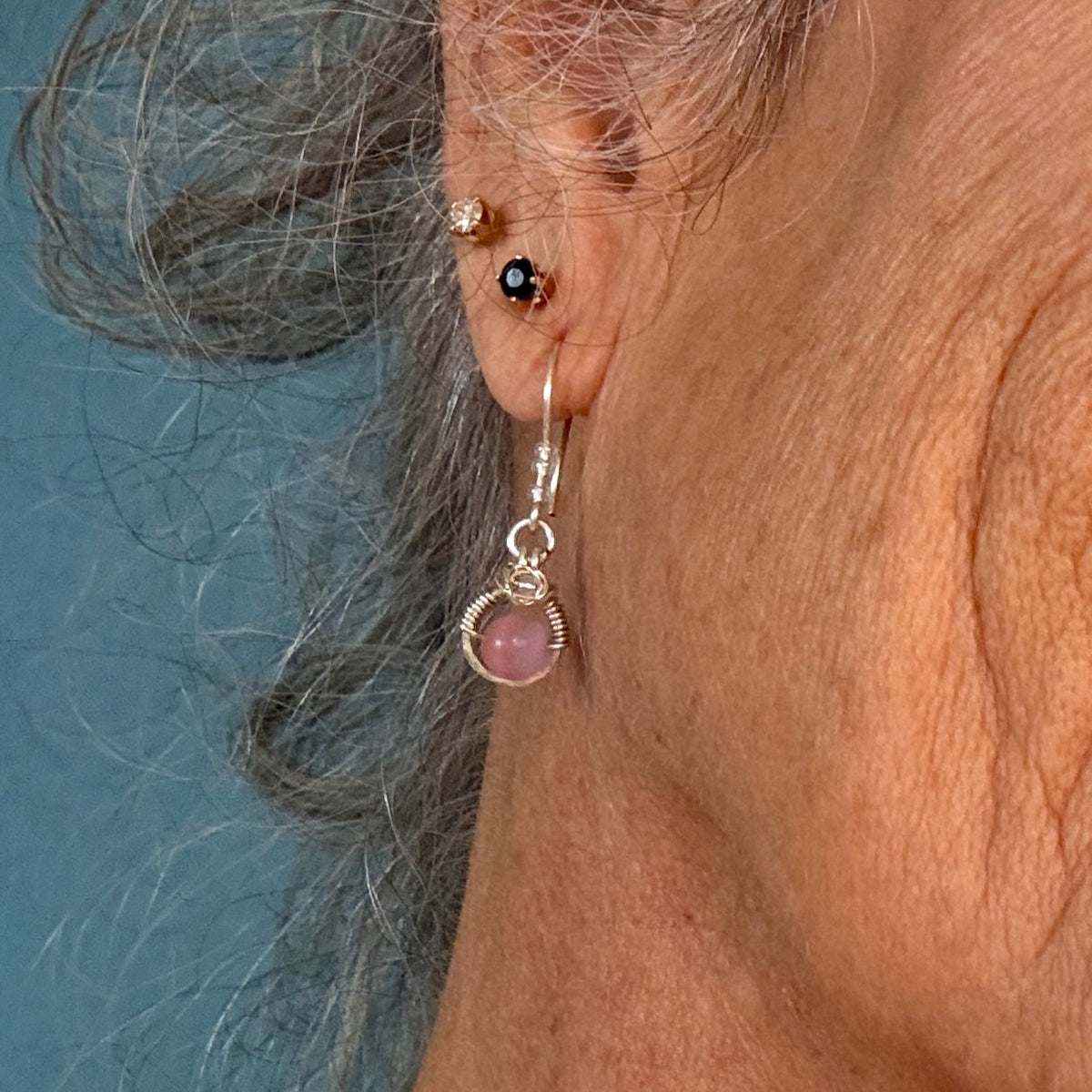 Pink cat’s eye drop earring with silver wire halo and hammered ear wire shown worn on ear