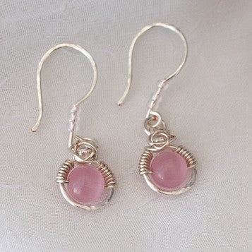 Handmade pink cat's eye earrings with 6mm round pink cat's eye bead in silver-plated wire halo, Miyuki iridescent light pink seed bead accents, and hammered silver-plated ear wires, displayed on light gray background