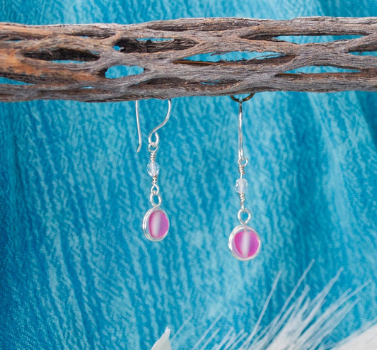 Pink mermaid glass earrings with double wire-wrapped bead and fire polished Czech accent hanging from driftwood with teal water background and pampas grass