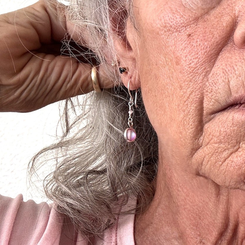 Pink mermaid glass earring with double wire-wrapped bead and crystal rondelle accent shown being placed on model with silver hair wearing a pink top