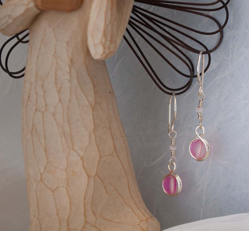 Pink mermaid glass earrings with double wire-wrapped bead and faceted crystal rondelle accent displayed on Willow Tree angel figurine against blue-gray background