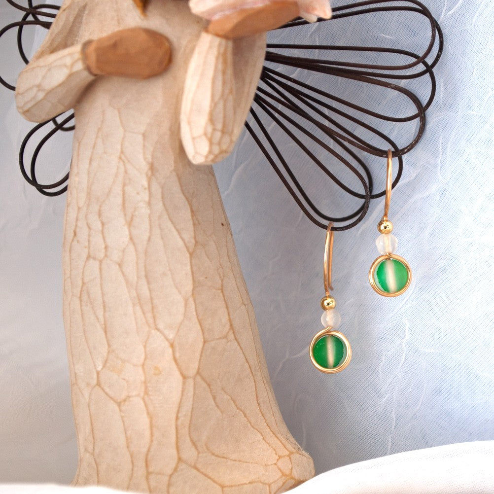 Pair of green mermaid glass drop earrings with white faceted agate beads hanging from a carved angel sculpture.
