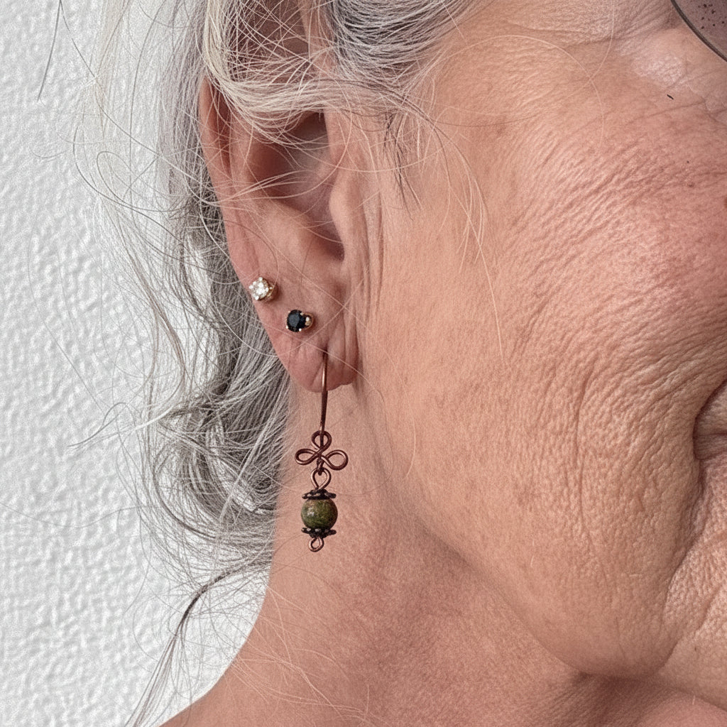 Handmade unakite gemstone drop earring with antique copper clover charm shown worn on model with silver hair.
