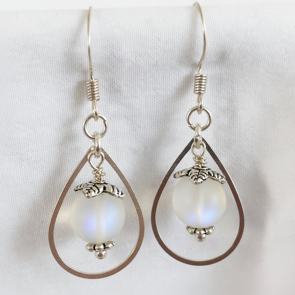 Close-up of handmade frosted mermaid glass drop earrings showing silver-tone teardrop frame, leaf bead cap, daisy spacer, and blue flash in the 8mm mermaid glass bead.