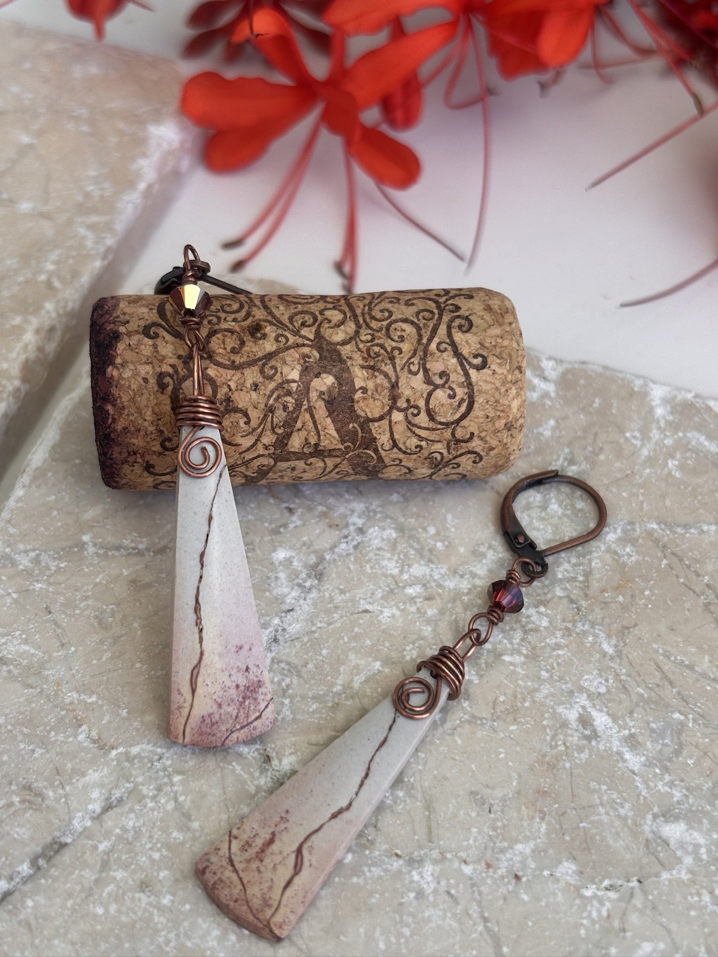 Handmade porcelain jasper drop earrings with antique copper wire wrap and Swarovski crystal charm, styled with decorative wine cork and red flowers on travertine stone.