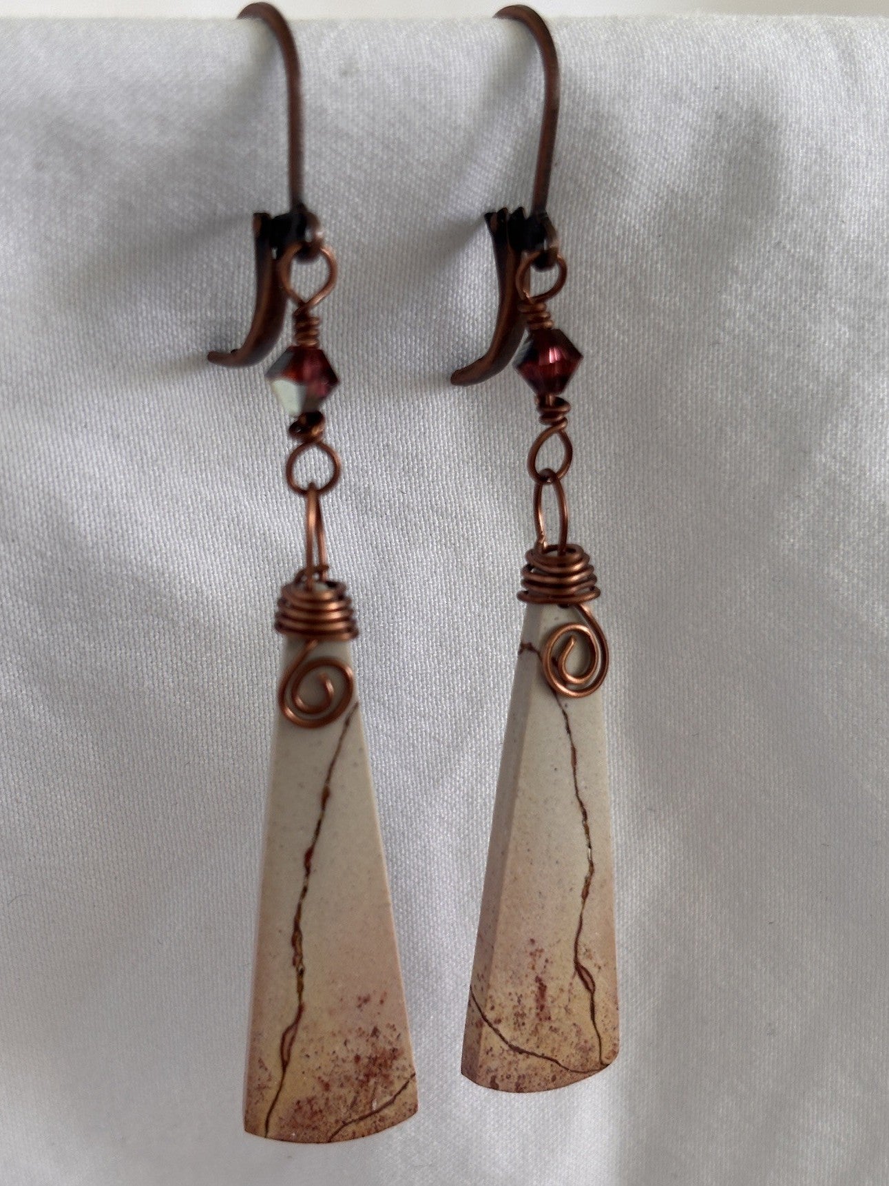 Pair of handmade porcelain jasper drop earrings with antique copper leverback ear wires, Swarovski crystal charms, and spiral wire wrap detail, displayed against white fabric.