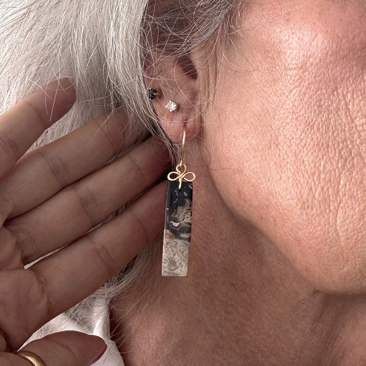 Petrified palm earring with brass handcrafted clover bail shown worn on model with silver hair, close-up view showing stone and bail detail