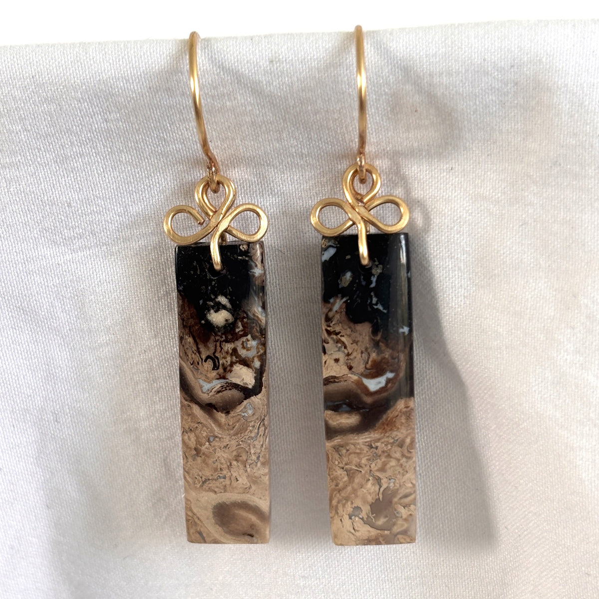 Handmade petrified palm earrings with brass handcrafted clover bail and ear wires showing black to cream stone gradient, displayed on white linen background