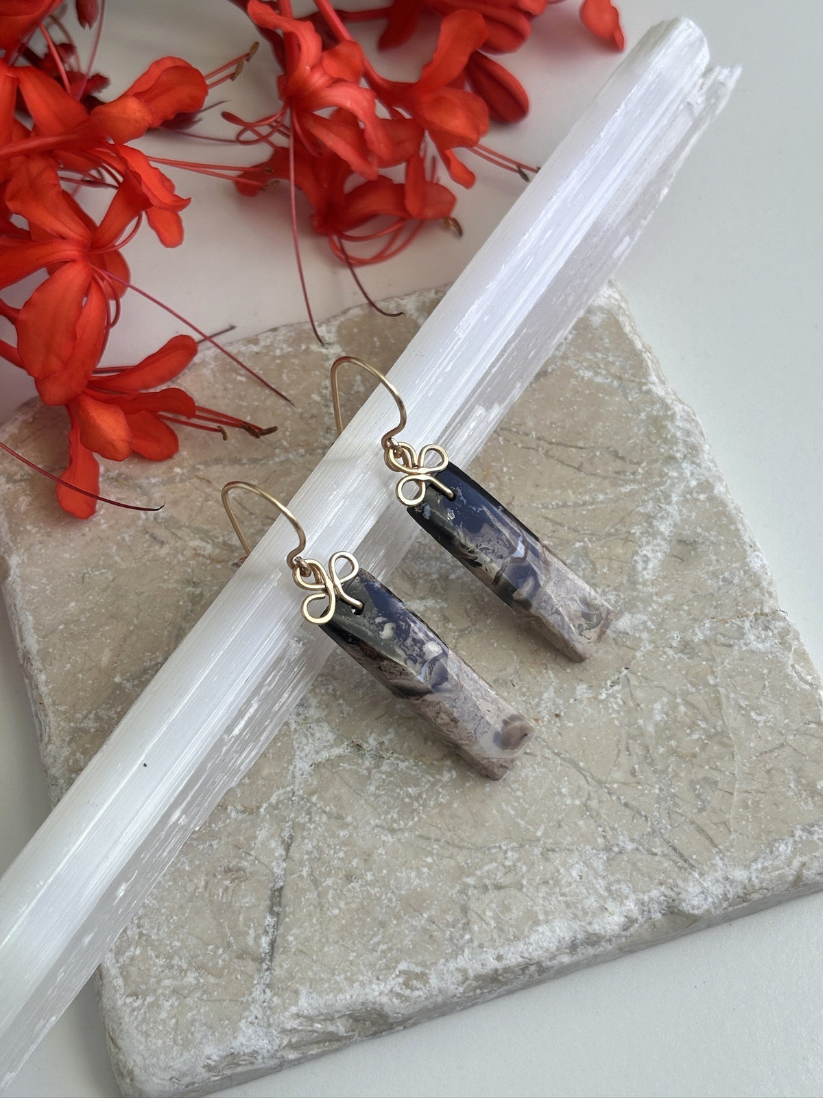 Petrified palm earrings with brass clover bail and ear wires displayed on selenite wand and travertine tile with red tropical flowers