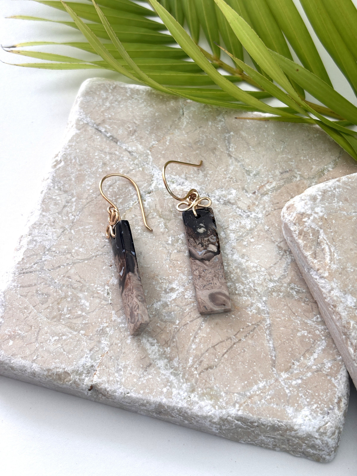 Pair of petrified palm earrings with brass handcrafted clover bail displayed on travertine tile with palm leaf