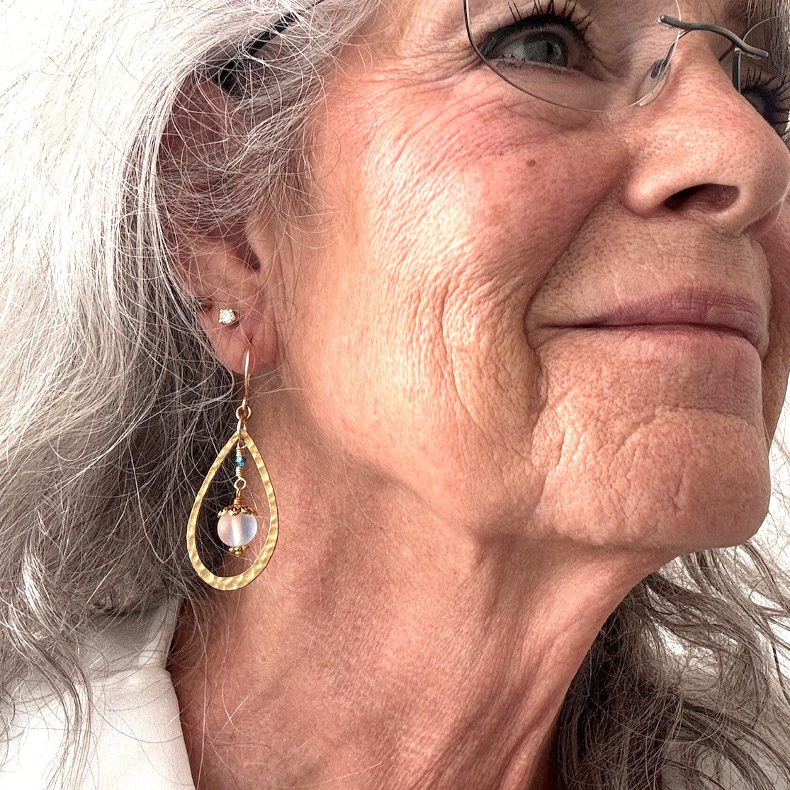 Mermaid glass earring with hammered brass teardrop frame and blue-green Swarovski bicone shown worn on model with silver hair