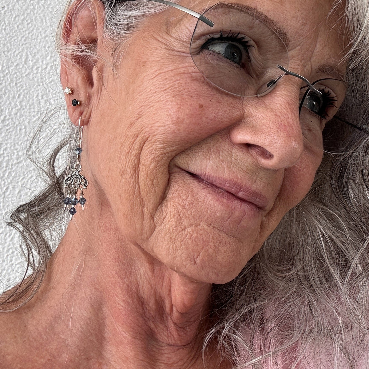 Blue iridescent Swarovski crystal chandelier earrings shown worn on model with silver hair and glasses, close-up showing chandelier scrollwork and crystal dangle detail