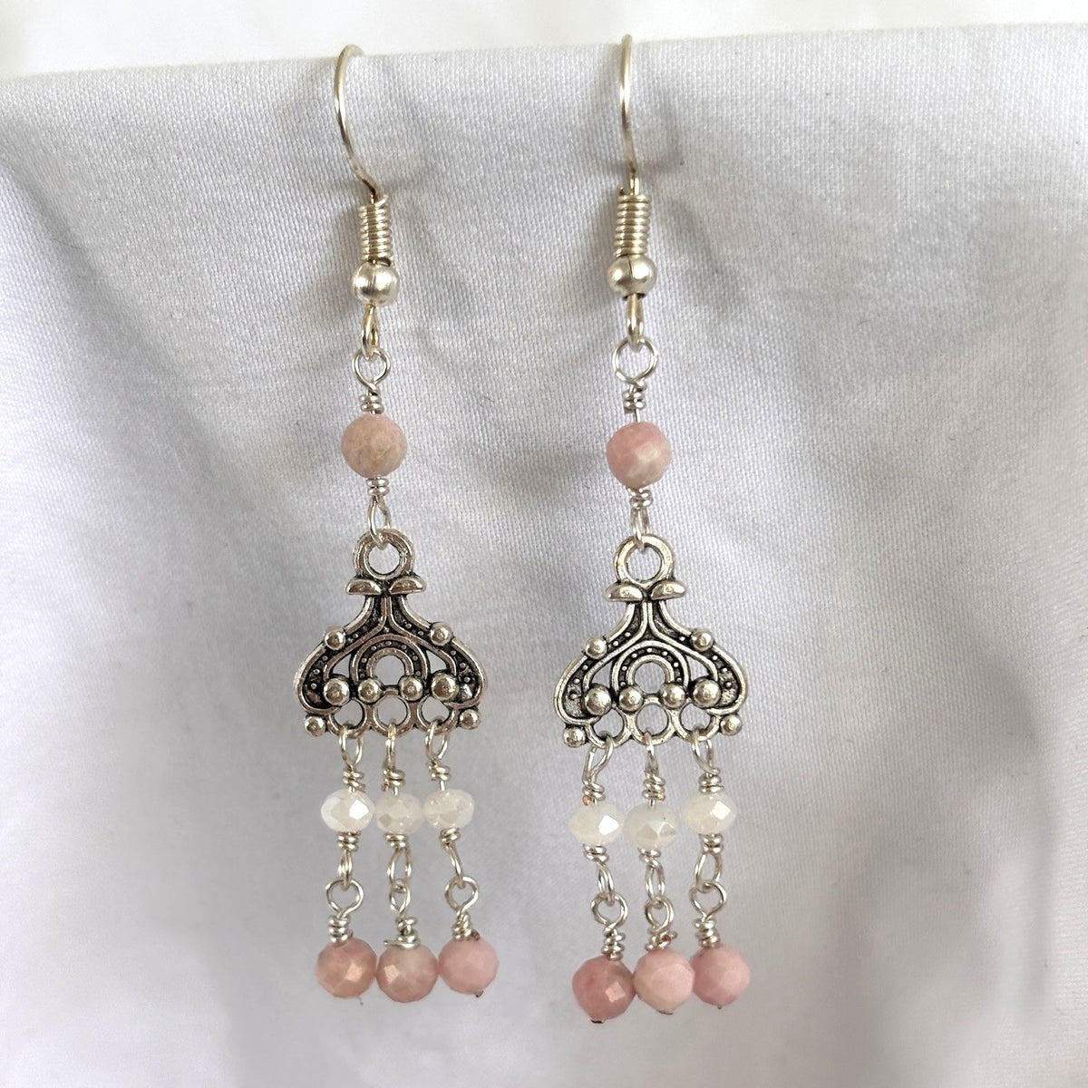 Handmade pink opal earrings with ornate silver-tone chandelier and three paddle dangles each beaded with a white crystal rondelle and faceted pink opal bead, displayed against white linen background