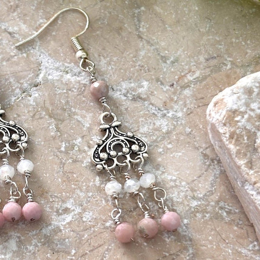 Close-up of pink opal chandelier earring showing ornate silver-tone filigree chandelier component, white crystal rondelle and pink opal bead paddle sequence, and faceted pink opal accent at ear wire