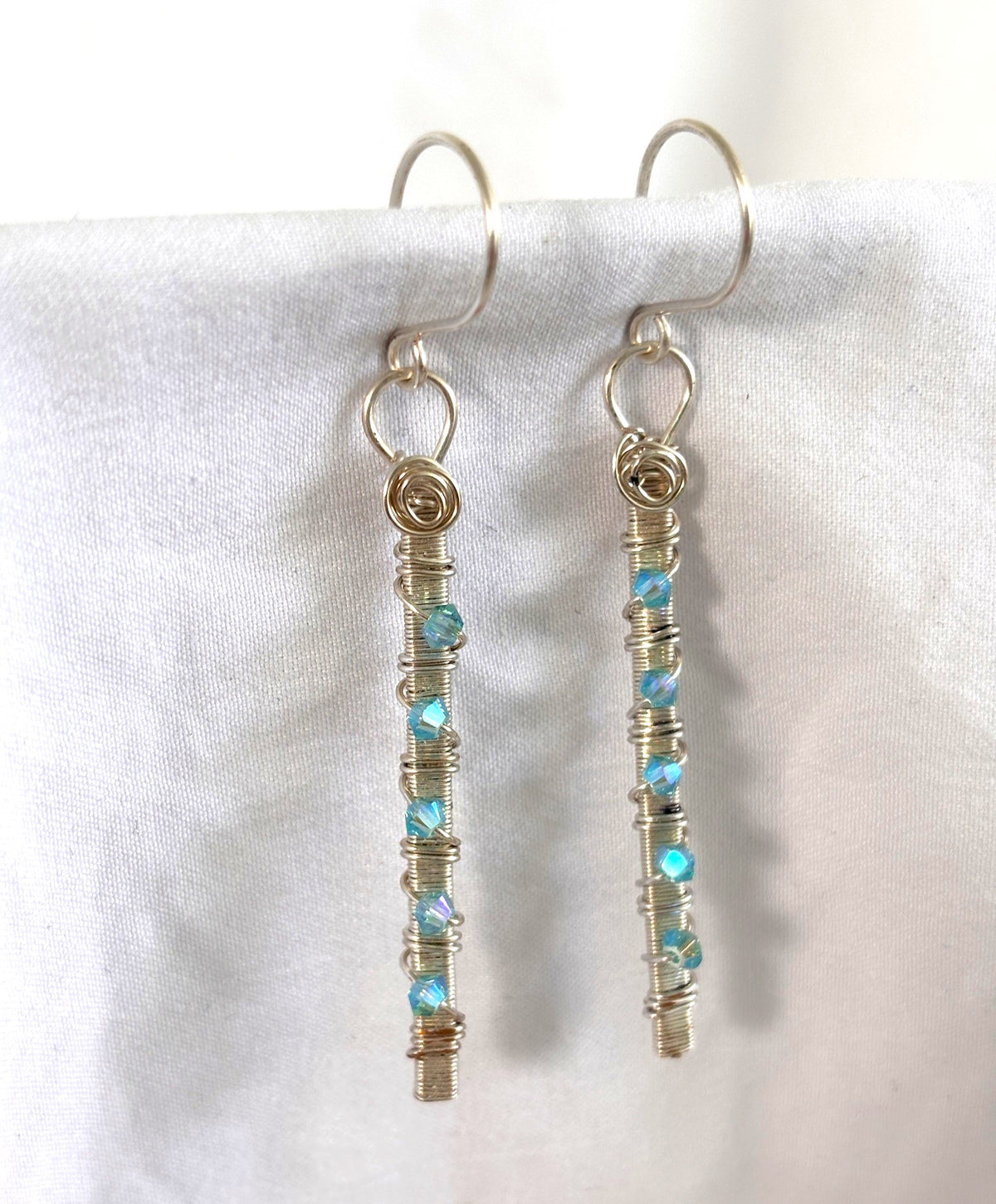 Handmade aqua Swarovski crystal earrings with hand wire-wrapped silver-plate bar and hand-coiled connecting ring on silver-plate ear wires, displayed against white linen background