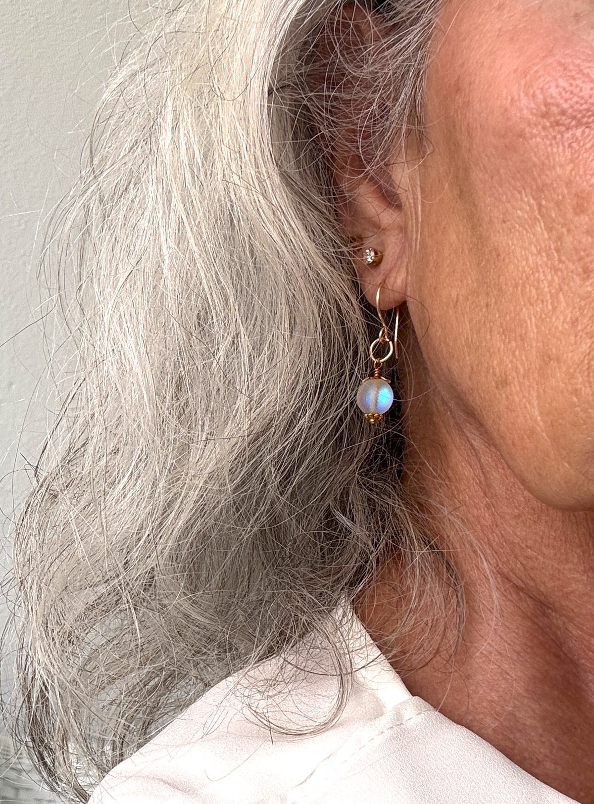 Frosted mermaid glass earrings with iridescent bead, gold-tone bead cap and daisy spacer, and oversized brass jump ring shown worn on model with silver hair and white top