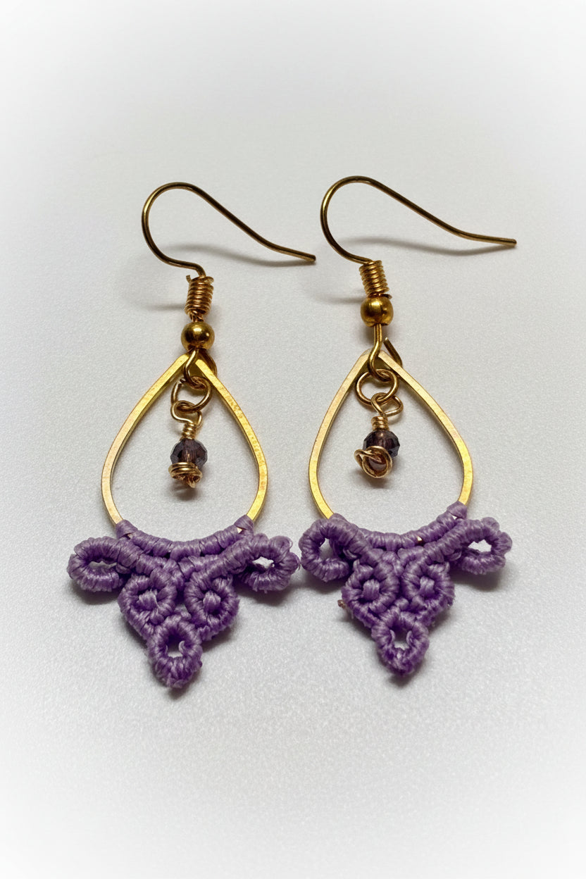 Close-up of handmade lavender macrame fan knotwork detail showing intricate scalloped arches and looped clusters on gold-tone teardrop hoop earrings.
