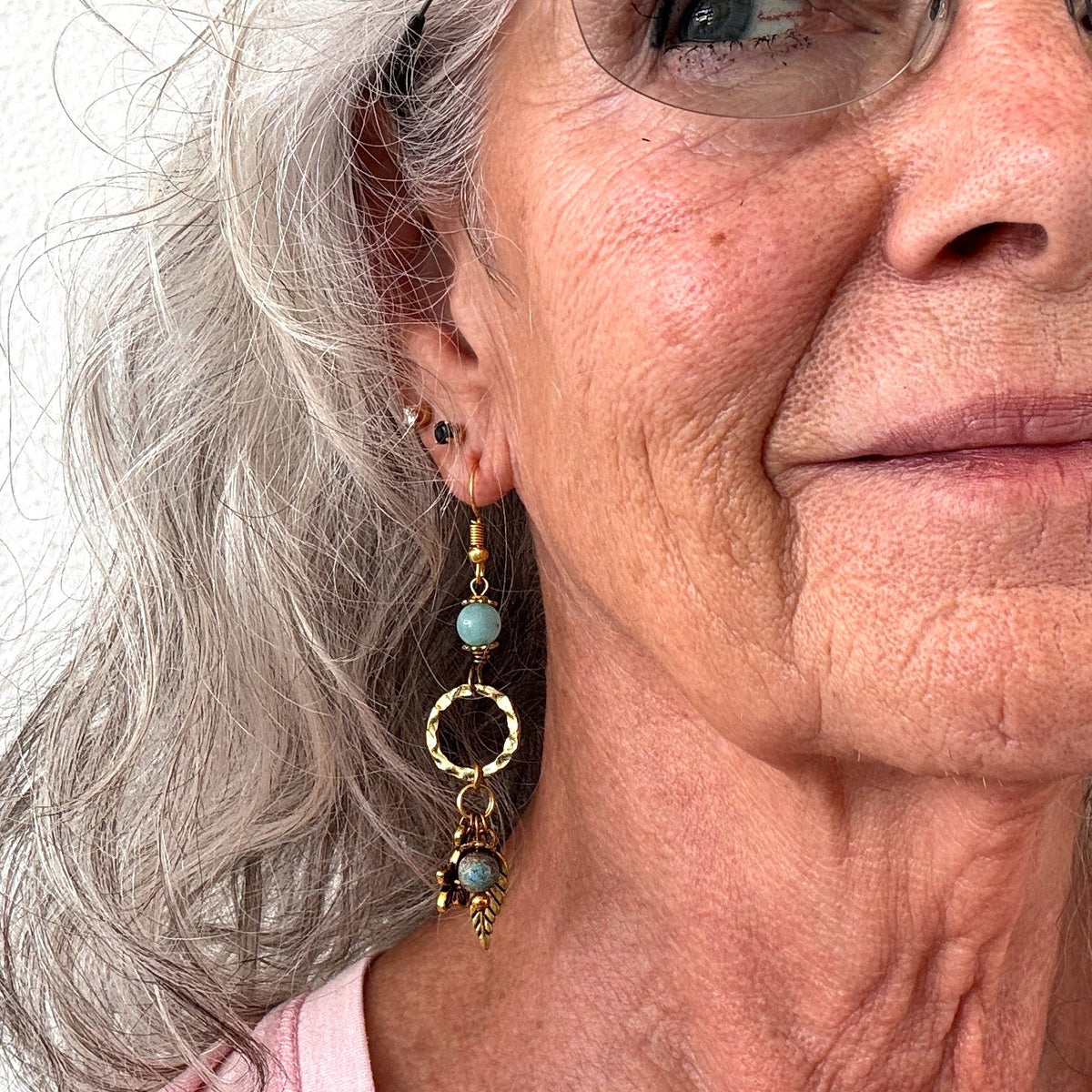 Gold-tone textured ring earring with amazonite bead, blue calsilica drop, and gold-tone leaf and flower charms shown worn on model with silver hair