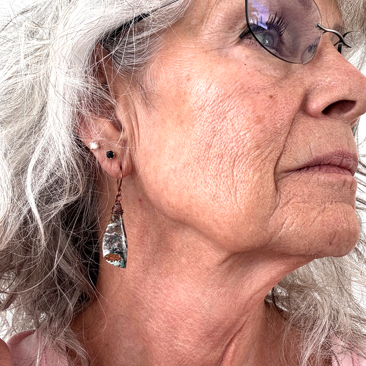 Wire-wrapped ocean jasper earring with copper wire wrapping and handcrafted copper ear wire shown worn on model with silver hair
