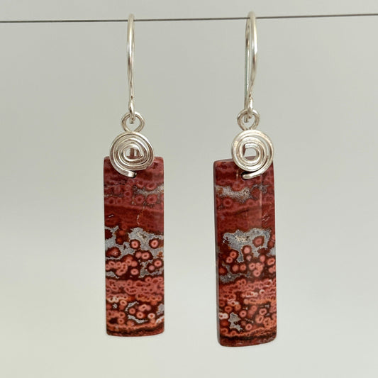 Handmade brecciated jasper earrings with silver-tone handcrafted swirl bail and hammered ear wires, hanging against a neutral gray background showing full stone and bail detail
